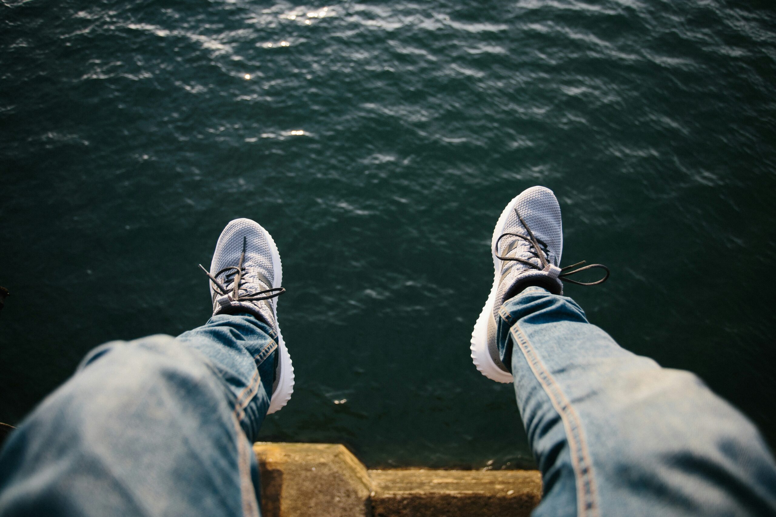 A man's legs over a lake. Representing the need to slow down and focus on self-care.
